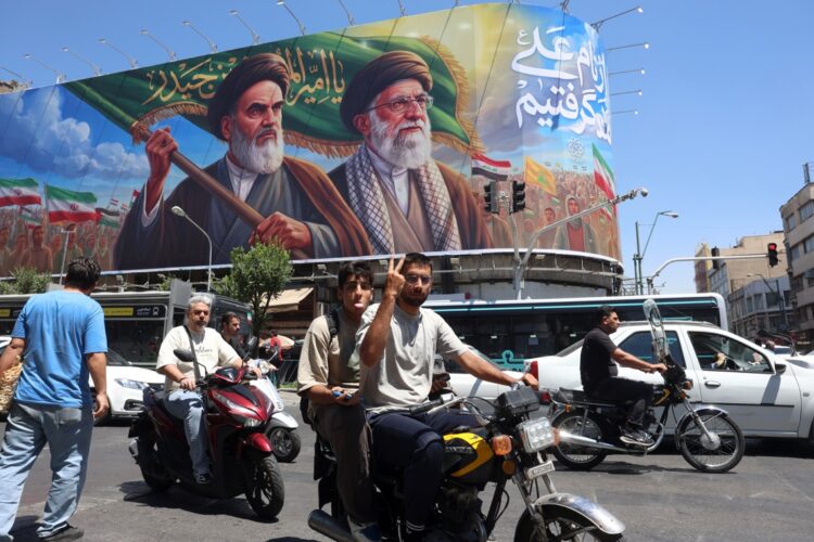 Un iraní hace el signo de la victoria mientras pasa en coche junto a una valla publicitaria de los difuntos líderes supremos iraníes, el ayatolá Ruhollah Khomeini y el ayatolá Ali Khamenei, en una calle de Teherán, Irán, el 15 de junio de 2026. Foto: EFE/EPA/ABEDIN TAHERKENAREH.
