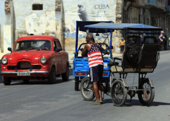 Un hombre vestido con una camiseta de la bandera de EE.UU., empuja un bicitaxi en La Habana. Foto: Ernesto Mastrascusa / EFE.