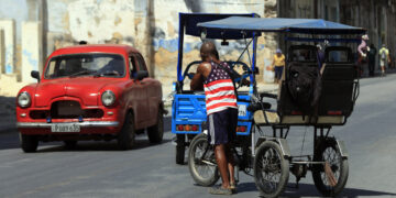 Un hombre vestido con una camiseta de la bandera de EE.UU., empuja un bicitaxi en La Habana. Foto: Ernesto Mastrascusa / EFE.