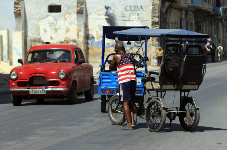 Un hombre vestido con una camiseta de la bandera de EE.UU., empuja un bicitaxi en La Habana. Foto: Ernesto Mastrascusa / EFE.