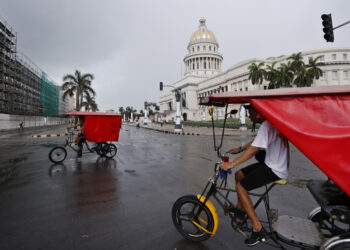 Personas pasan en bicitaxis frente al Capitolio de La Habana. Foto:  Ernesto Mastrascusa/EFE.