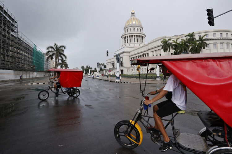 Personas pasan en bicitaxis frente al Capitolio de La Habana. Foto: Ernesto Mastrascusa/EFE.