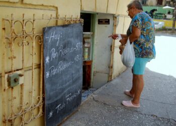 Una mujer observa la pizarra de precios en una bodeguita privada en La Habana, en agosto de 2026. Foto: AMD.