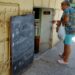 Una mujer observa la pizarra de precios en una bodeguita privada en La Habana, en agosto de 2026. Foto: AMD.