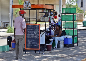 Un hombre mira la pizarra de precios de un puesto de comida en una calle en La Habana. Foto: Ernesto Mastrascusa / EFE.
