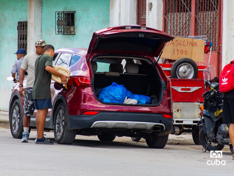 Dos hombres echan gasolina en un auto, junto a un punto de venta informal, en La Habana. Foto: Otmaro Rodríguez.