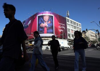 Personas caminan por las calles de Teherán mientras una valla muestra una imagen de Trump, al fondo.. Foto: ABEDIN TAHERKENAREH/EFE/EPA.