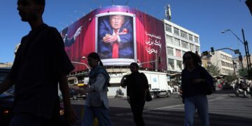Personas caminan por las calles de Teherán mientras una valla muestra una imagen de Trump, al fondo.. Foto: ABEDIN TAHERKENAREH/EFE/EPA.
