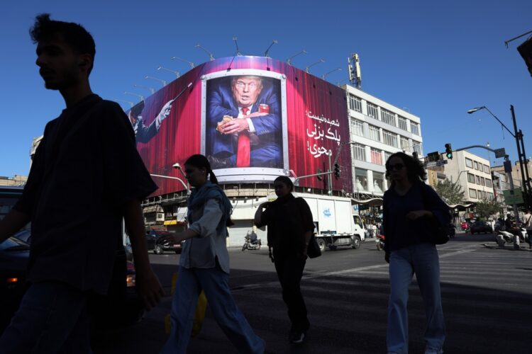 Personas caminan por las calles de Teherán mientras una valla muestra una imagen de Trump, al fondo.. Foto: ABEDIN TAHERKENAREH/EFE/EPA.
