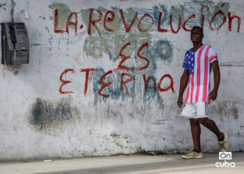 Un hombre con un pulóver de la bandera de EE.UU. pasa junto a un grafiti revolucionario en una calle de La Habana. Foto: Otmaro Rodríguez.
