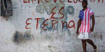 Un hombre con un pulóver de la bandera de EE.UU. pasa junto a un grafiti revolucionario en una calle de La Habana. Foto: Otmaro Rodríguez.