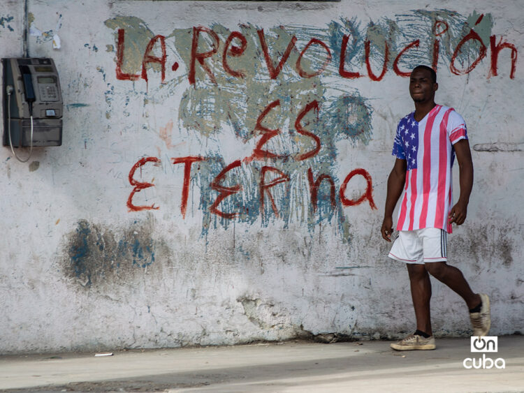 Un hombre con un pulóver de la bandera de EE.UU. pasa junto a un grafiti revolucionario en una calle de La Habana. Foto: Otmaro Rodríguez.