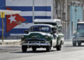 Vehículos antiguos transitan frente a un mural con la bandera de Cuba pintada. Foto: EFE/Ernesto Mastrascusa.