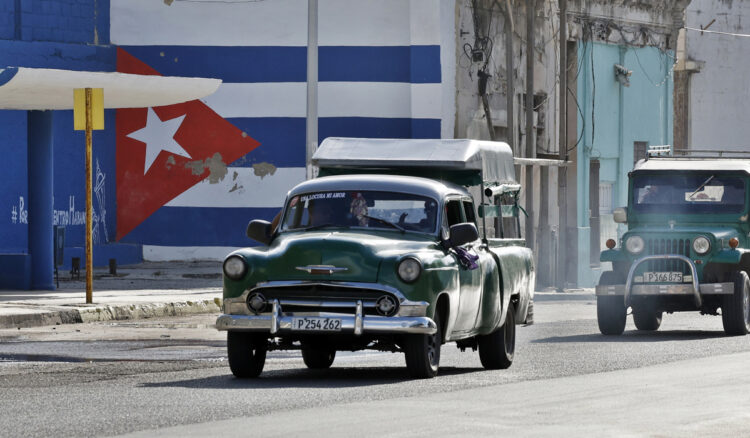 Vehículos antiguos transitan frente a un mural con la bandera de Cuba pintada. Foto: EFE/Ernesto Mastrascusa.