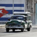 Vehículos antiguos transitan frente a un mural con la bandera de Cuba pintada. Foto: EFE/Ernesto Mastrascusa.