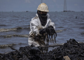 Fotografía del 29 de septiembre de 2026 de una empleada pública en una jornada de limpieza de petróleo derramado en una orilla del lago de Maracaibo. Foto: EFE/ Henry Chirinos.