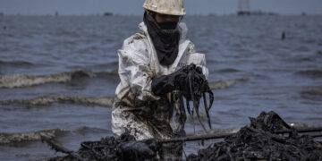 Fotografía del 29 de septiembre de 2026 de una empleada pública en una jornada de limpieza de petróleo derramado en una orilla del lago de Maracaibo. Foto: EFE/ Henry Chirinos.
