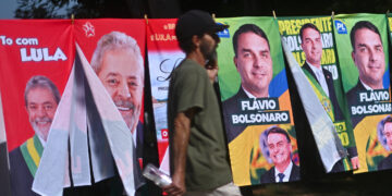 Un hombre camina frente a una tienda informal de banderas con la imagen del presidente de Brasil y candidato a la reelección, Luiz Inácio Lula da Silva y del candidato presidencial, Flávio Bolsonaro. Foto: EFE/Andre Borges.