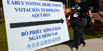 Una mujer camina junto a un cartel informativo durante la jornada de votación anticipada el lunes 19 de octubre en Houston, Texas. Foto: EFE/ Carlos Ramírez.