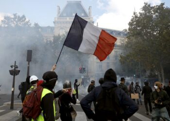 Manifestantes sostienen una bandera francesa mientras participan en una protesta contra el aumento del costo de vida y los recortes en los servicios públicos en la plaza de la República, en París, el 17 de octubre de 2026. Foto: EFE/EPA/MOHAMMED BADRA.